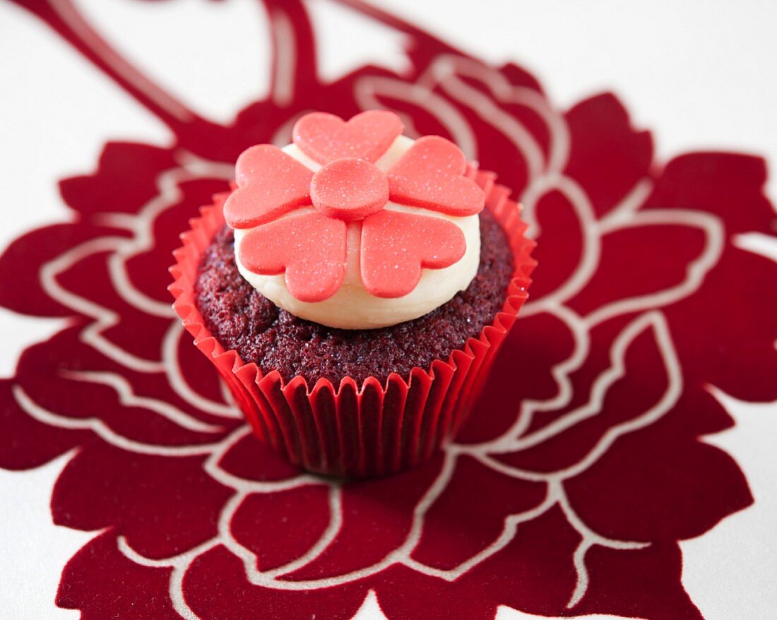 A red velvet cupcake decorated with red fondant flowers
