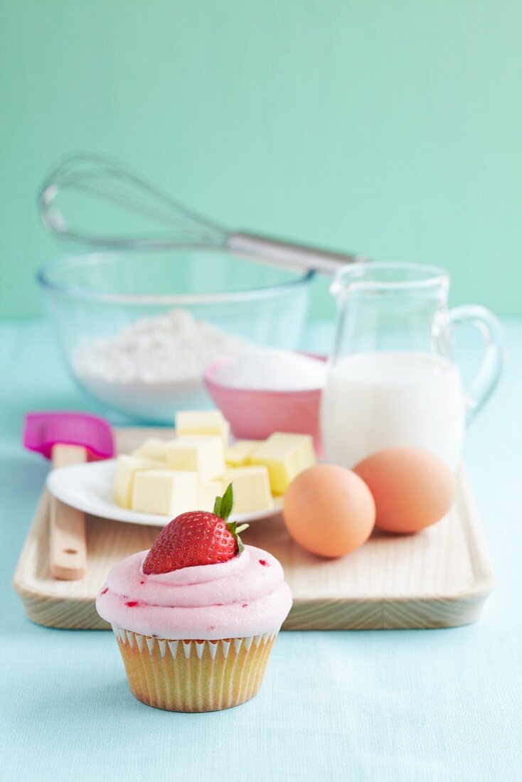 A strawberry cupcake with baking ingredients