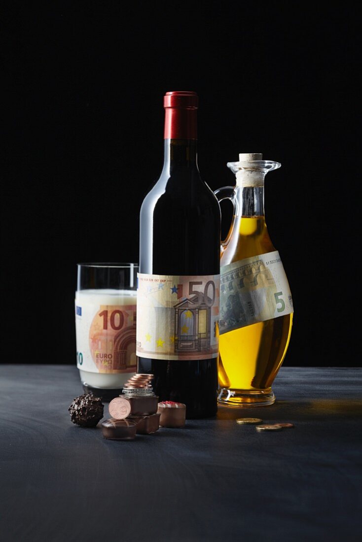 A symbolic image of a gourmet investment: pralines, red wine, milk and olive oil with money