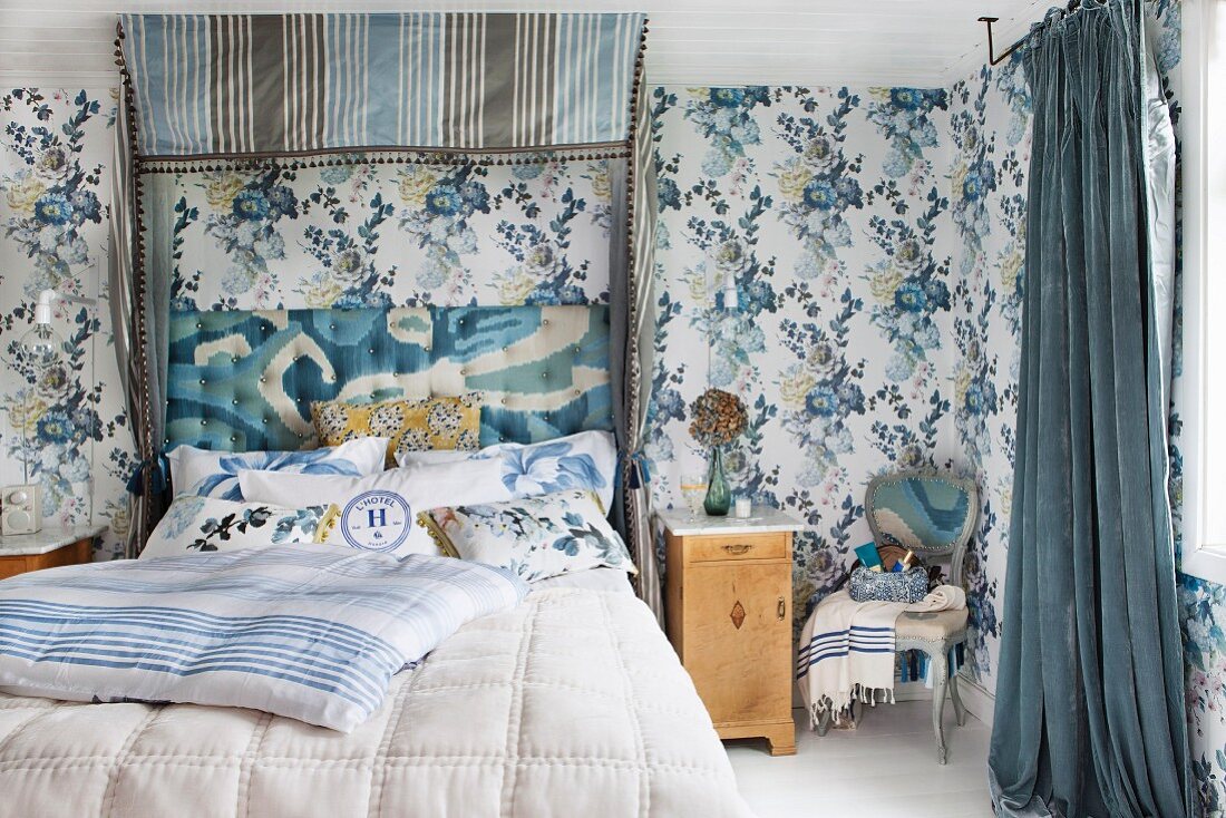 Half-tester double bed with upholstered headboard and blue and grey striped canopy in bedroom with blue floral wallpaper