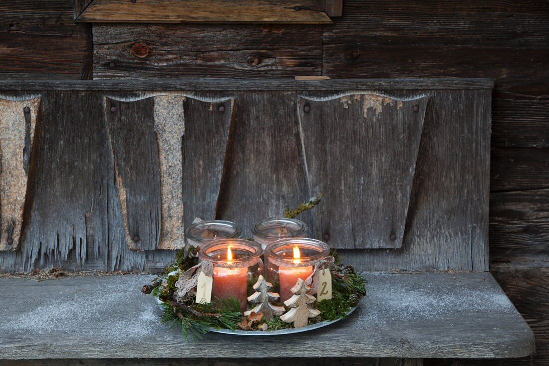 Rustikaler Adventskranz mit zwei brennenden Kerzen in Weckgläsern auf einer verwitterten Holzbank