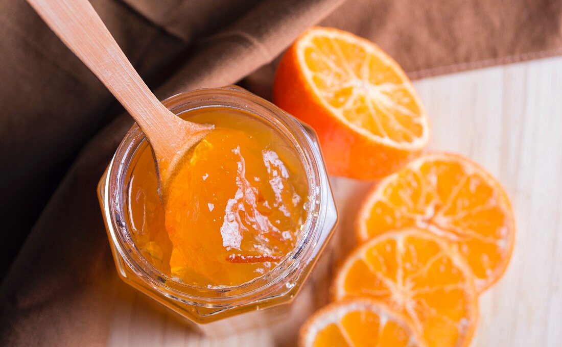 Ein Glas Orangenmarmelade und frische halbe Orangen