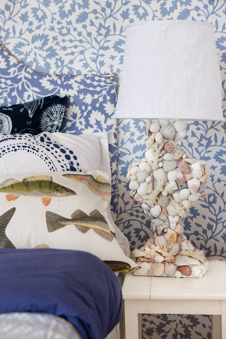Maritime bedroom with fish-patterned bed linen and lamp base covered in seashells