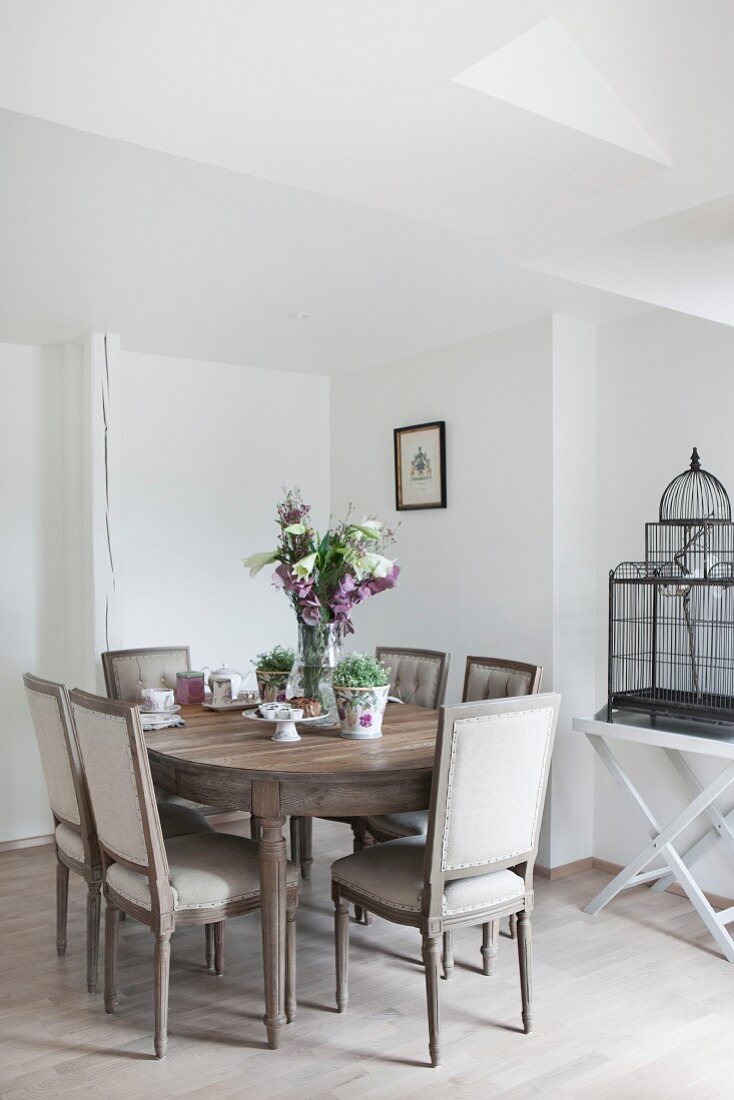 Wooden dining table, antique upholstered chairs and vintage birdcage on tray table in dining room