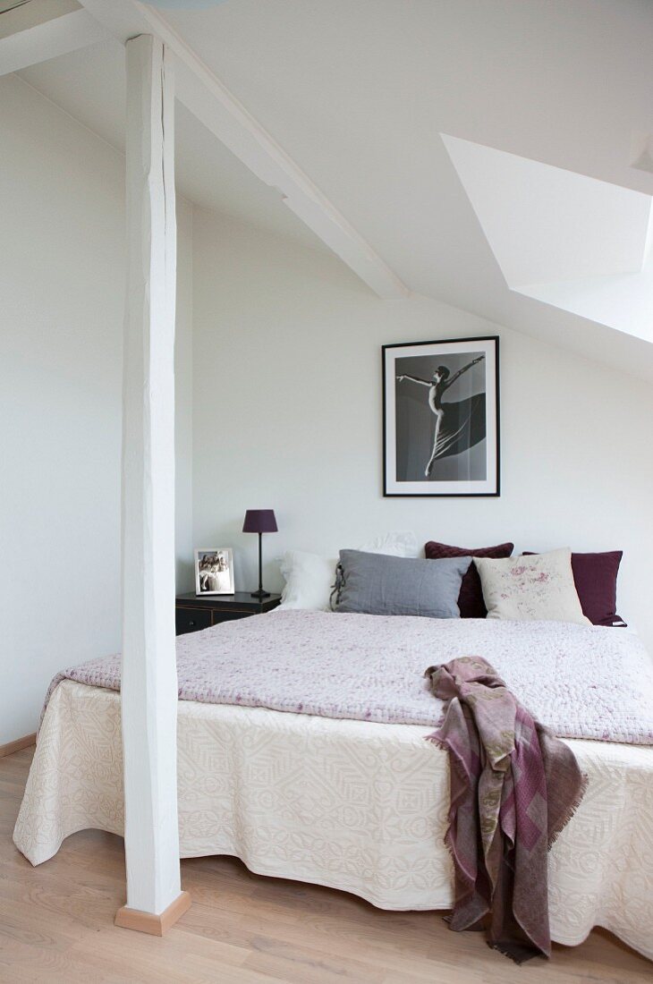 Double bed with bedspread in corner of room under sloping ceiling