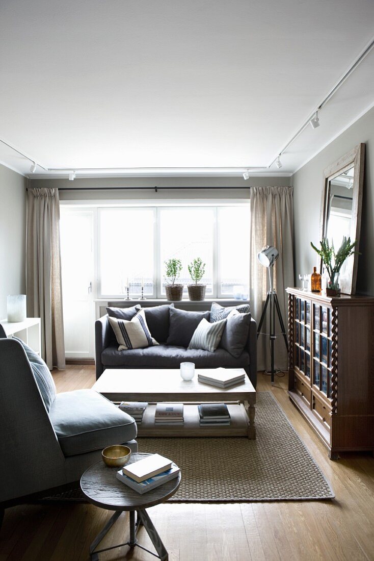 Armchair and sofa around pale coffee table; traditional, half-height display case and retro-style standard lamp to one side