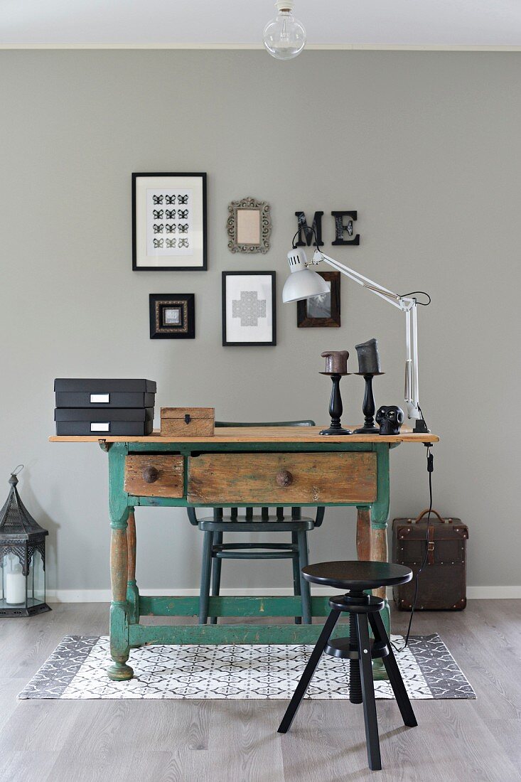 Black swivel stool and rustic wooden table with peeling paint against pale grey wall