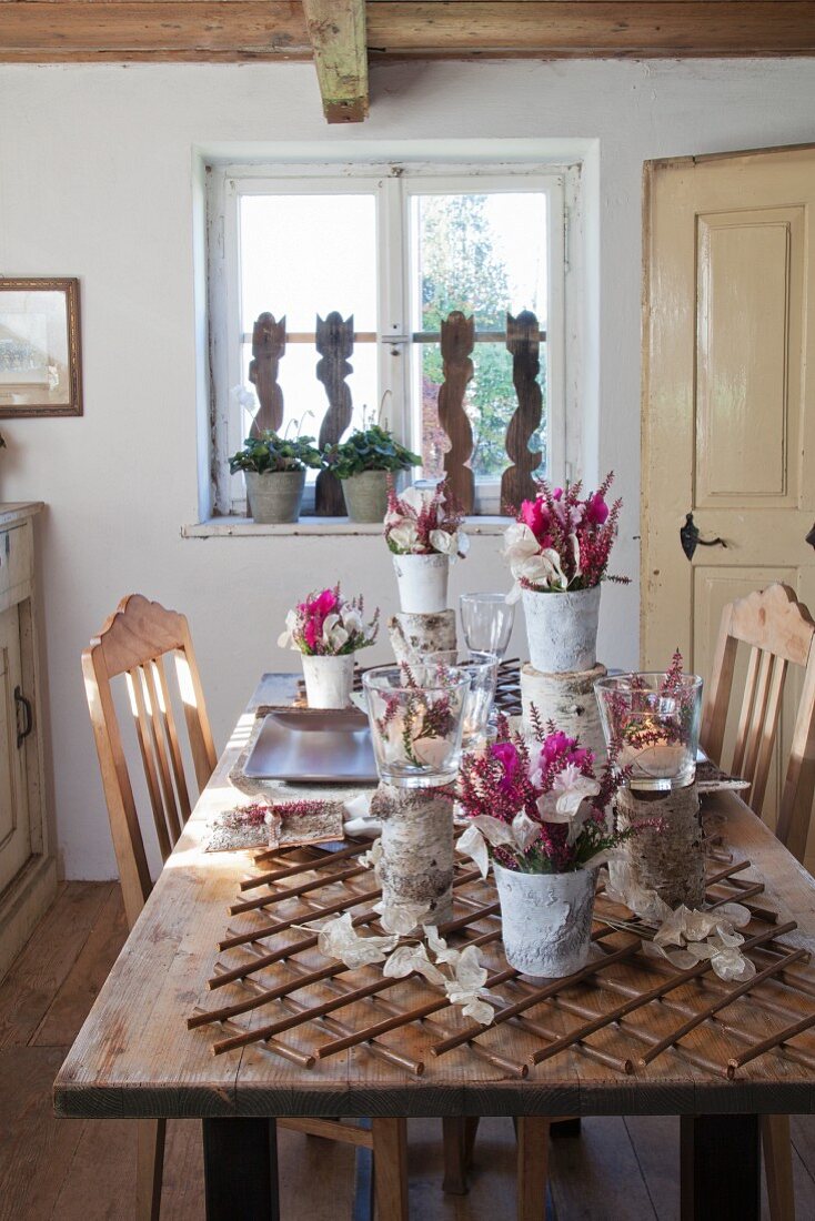 Vases and flowers arranged with natural materials on rustic table in simple dining room