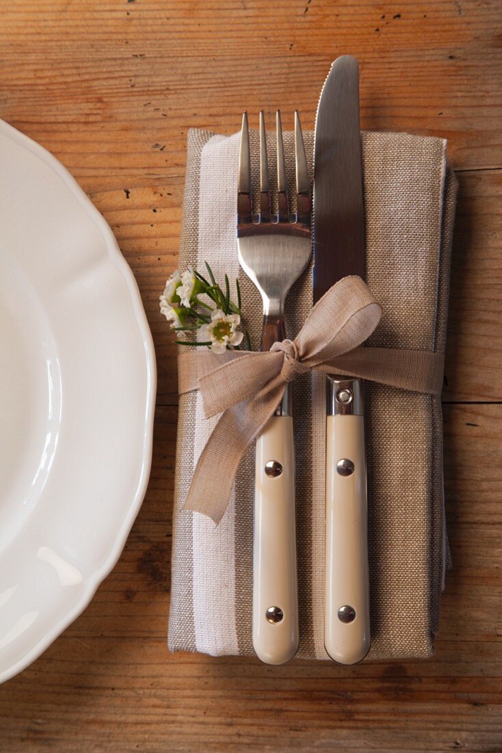 Cutlery and linen napkin tied with ribbon and decorated with waxflowers