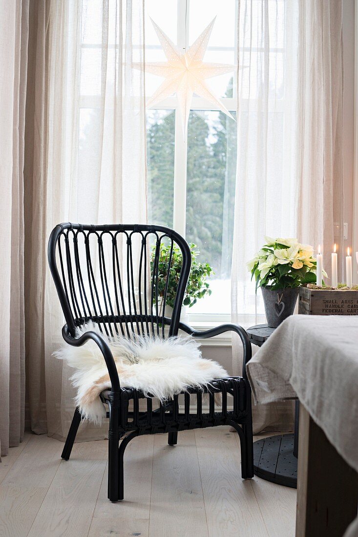 Black cane chair with white fur blanket below star ornament hanging in window