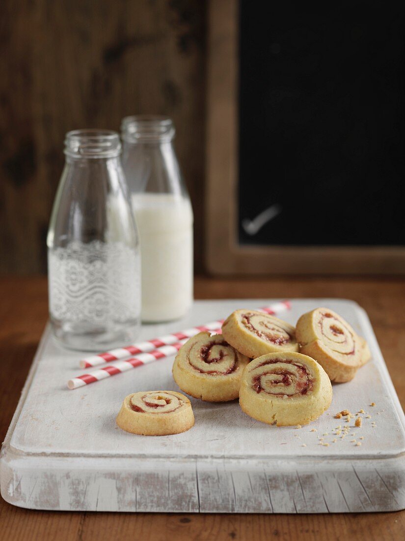 Swiss roll, sliced, and bottles of milk on a wooden board