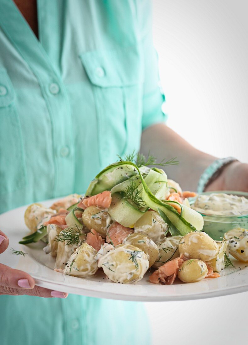 A woman serving a large plate of salmon, potatoes, cucumber and Tartare sauce