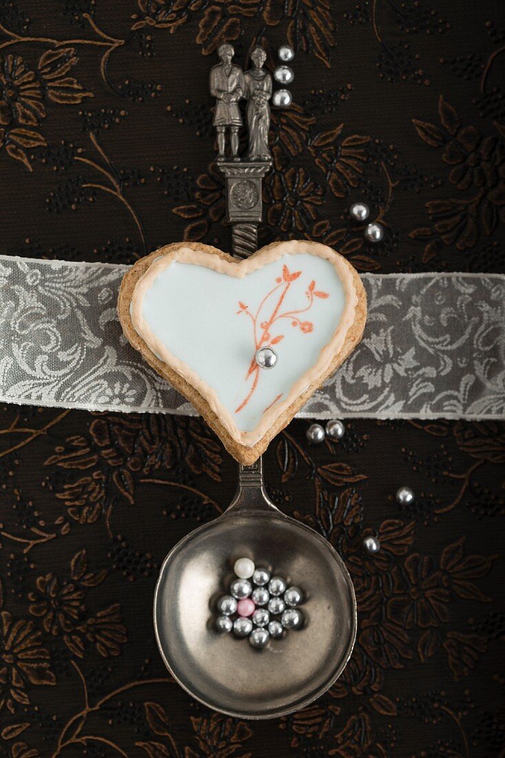 A heart-shaped biscuit with an egg white glaze and a stamped motif on a spoon with a bridal couple