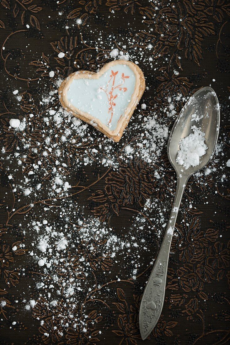 A heart-shaped biscuit, icing sugar and a spoon