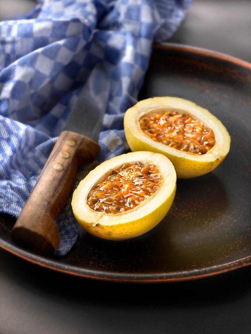 A passion fruit, halved, on a plate with a knife and a tea towel