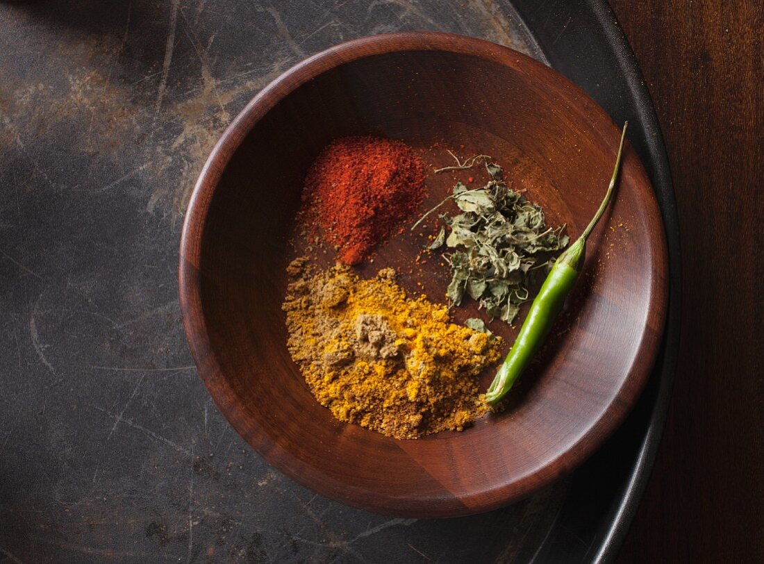 Indian spices and green chilli in a wood bowl (seen from above)