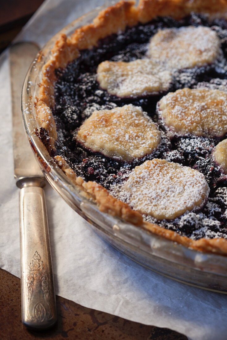 A mulberry pie with icing sugar topped with biscuits