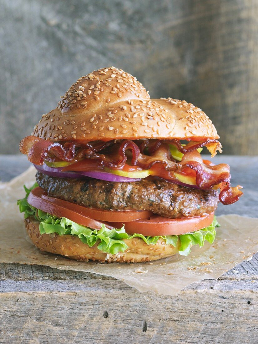 A hamburger with bacon, tomatoes and letters