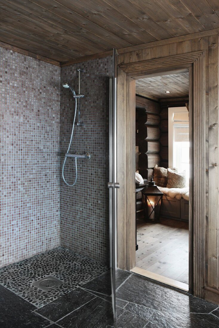 Floor-level shower with mosaic tiles next to open door with view of floor lantern in living area