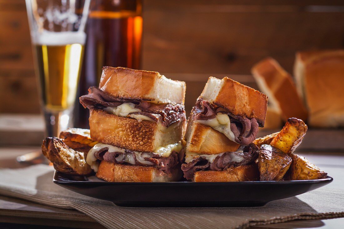Roast beef and cheese sandwiches with potato wedges and beer