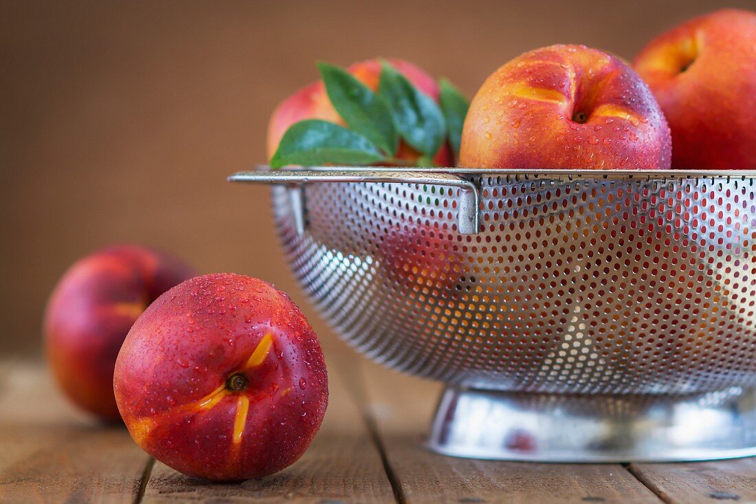 Freshly washed nectarines in a colander on a rustic wooden table