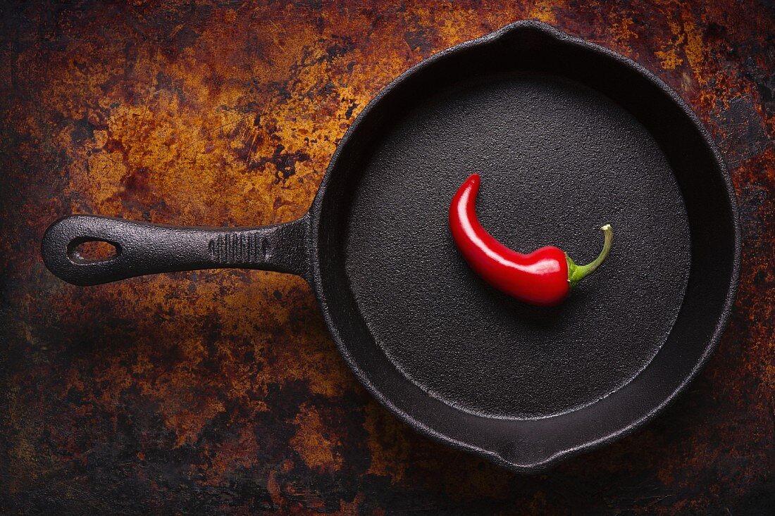 A single red chilli pepper in a cast iron pan (seen from above)
