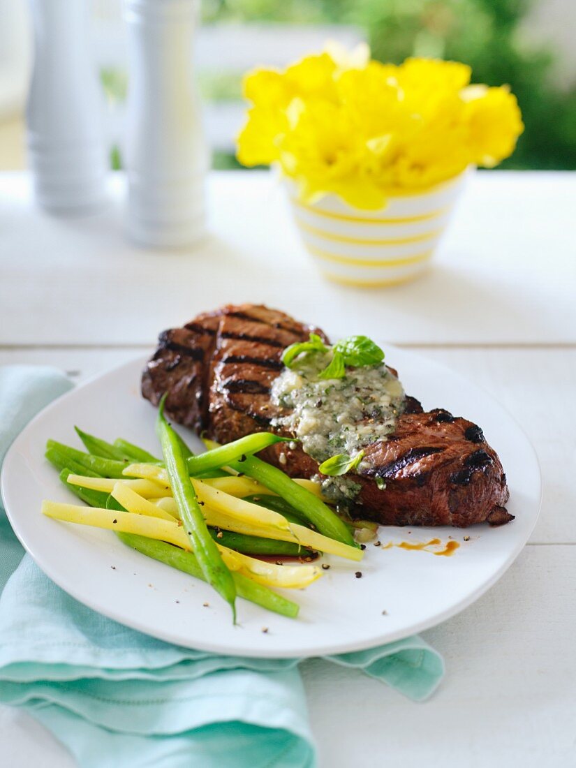 Gegrilltes Steak mit Blauschimmelkäsesauce und Bohnen auf Tisch mit Narzissenstrauss