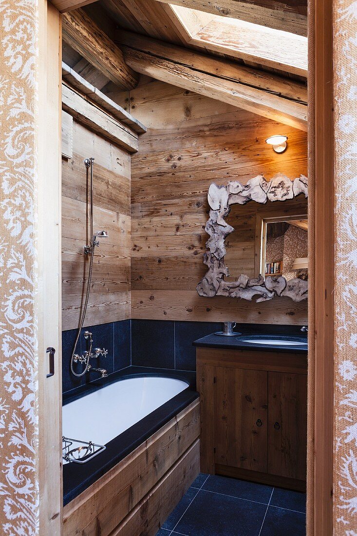 Holz und anthrazitfarbene Fliesen in rustikalem Badezimmer unterm Dach; Spiegel mit künstlerisch gestaltetem Rahmen
