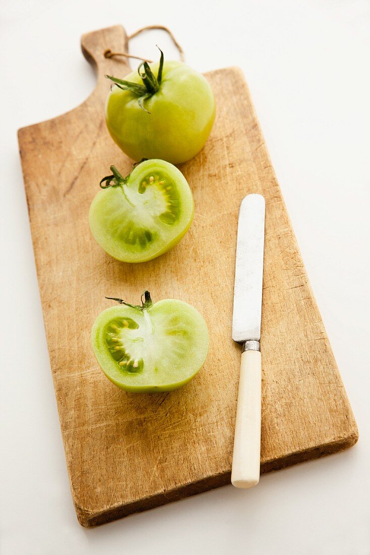 Green tomatoes, whole and halved, on a chopping board with a knife