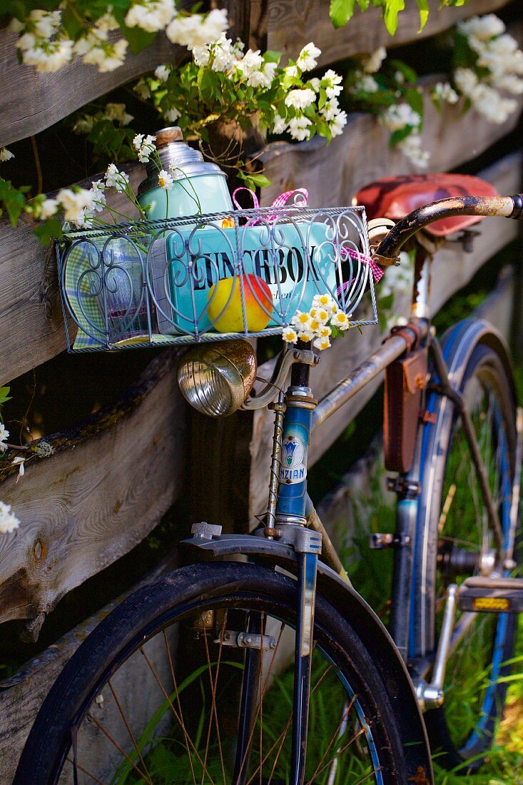 Old bicycle with picnic basket leaning against wooden fence