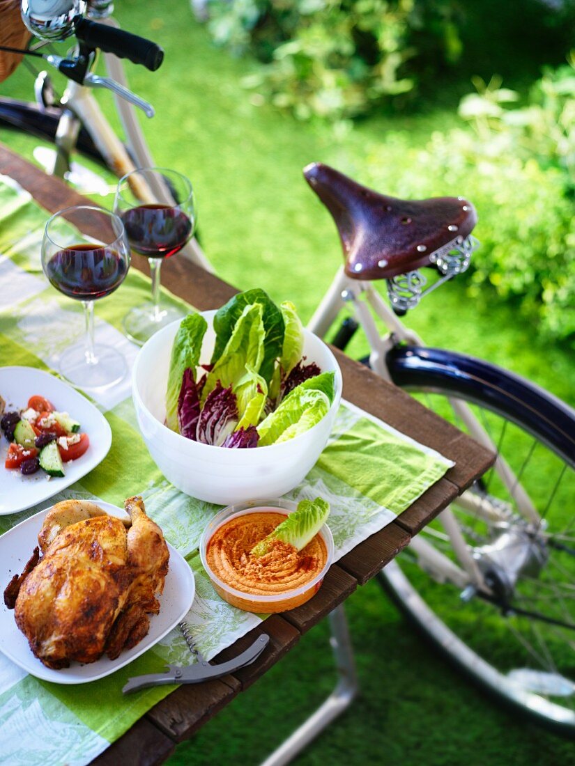 A bicycle picnic with chicken, a dip and salad in a park