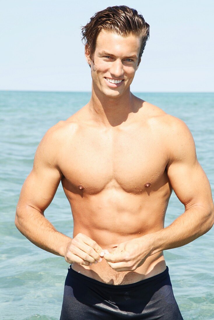 A muscular young man by the sea wearing blue bathing shorts