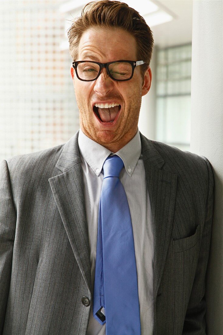 A man wearing glasses, a grey blazer and a tiny making a face: winking