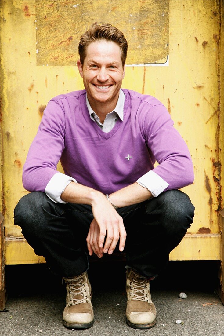 A man crouching down wearing a purple jumper and jeans
