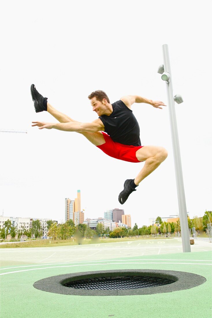 Mann beim Trampolin springen im Grünen vor Skyline