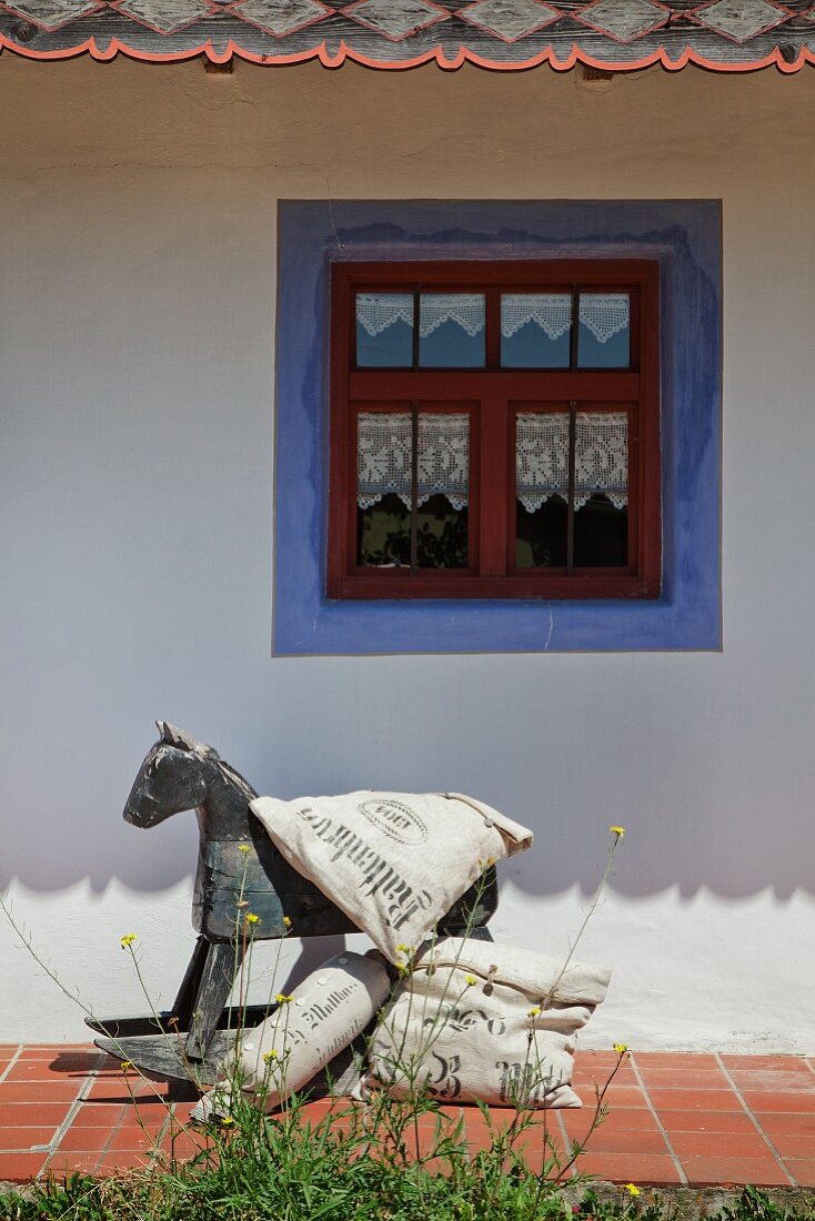 Vintage rocking horse and cushions with vintage-style lettering outside farmhouse with blue border around window