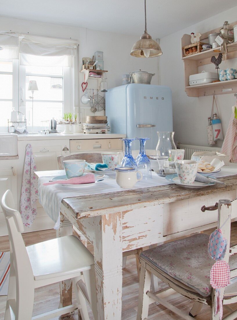 Dining table and chairs in vintage-style shabby-chic kitchen-dining room with pale blue fridge in background