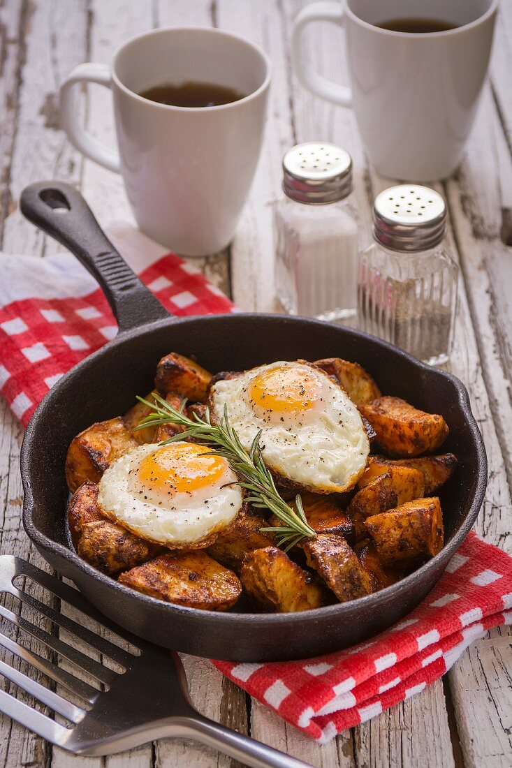 Spiced baked potatoes with fried eggs and rosemary in a cast iron pan