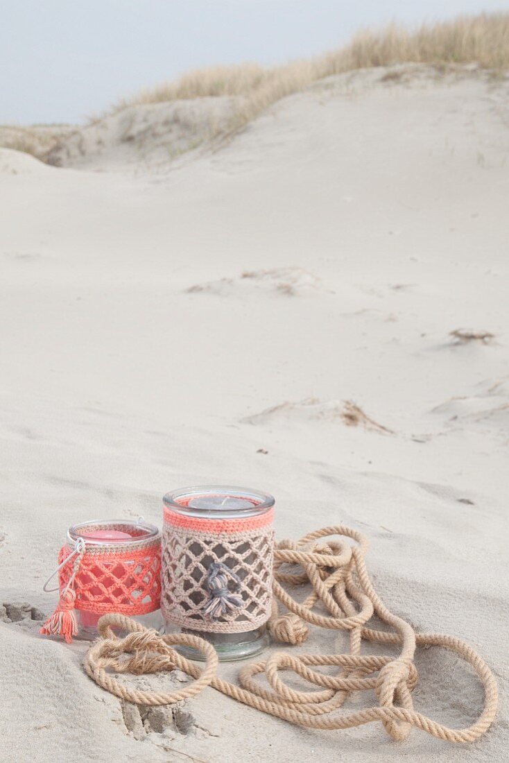 Candle lanterns in pastel crocheted covers on beach