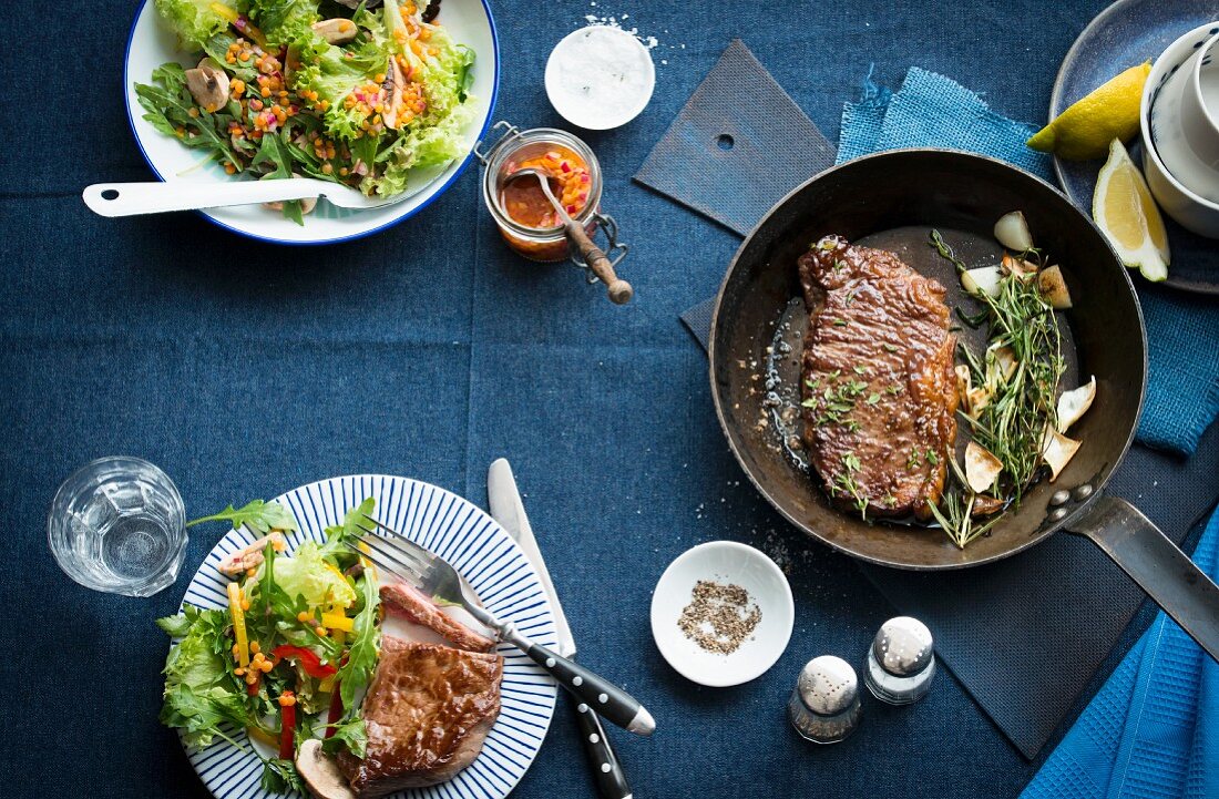 A steak in a pan with a side salad