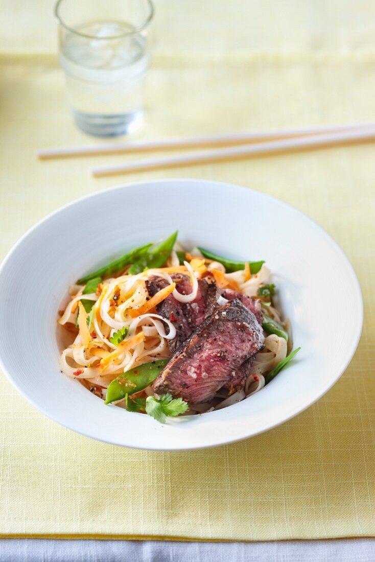 Grilled beef on a bed of rice noodles with mange tout, coriander and chilli flakes