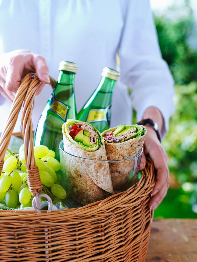 A woman holding a picnic basket with mineral water, grapes and freshly made wraps