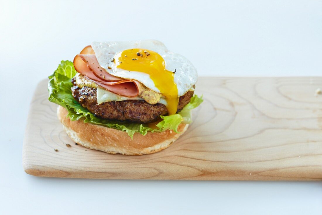 A hamburger with lettuce, ham, cheese and a fried egg