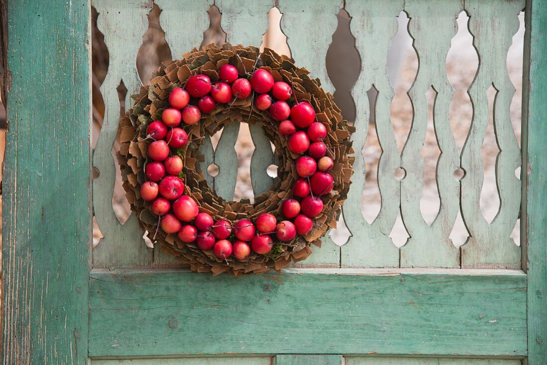 Wreath of bark and small red apples hung on weathered wooden door