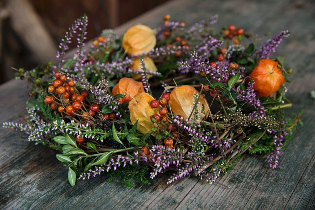 Kranz aus Lampionblumen, Heidekraut und Beerenzweigen auf Holz Untergrund