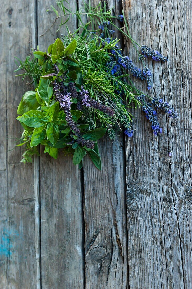 A bunch of fresh herbs with lavender flowers on a wooden surface