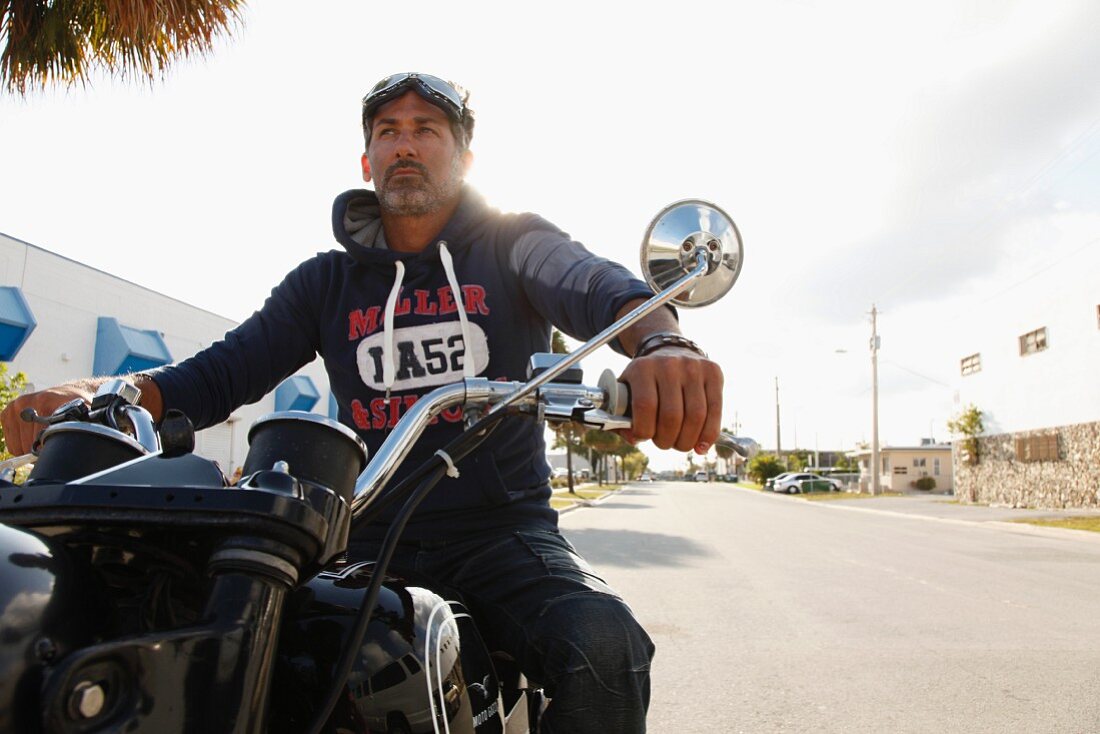 A man wearing a hooded sweatshirt sitting on a motorbike