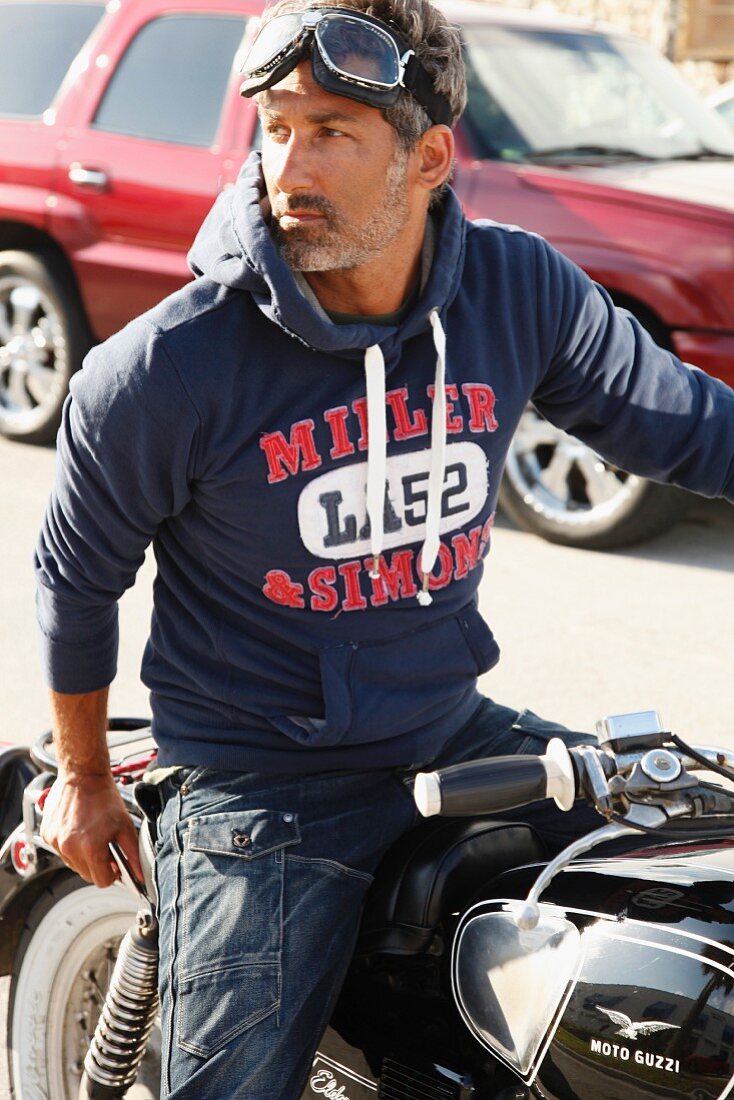 A man wearing a hooded sweatshirt sitting on a motorbike