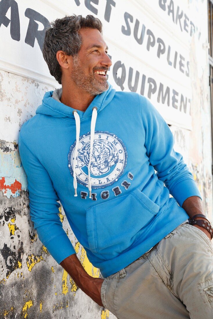 A man wearing a light-blue hooded sweatshirt leaning against a wall