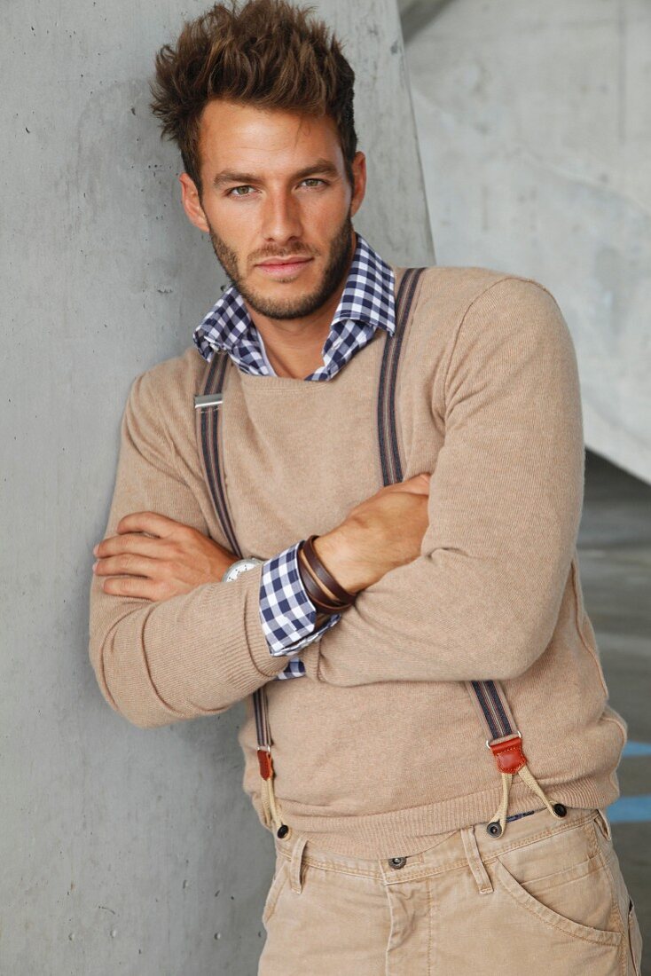 A young man wearing a checked shirt, a sand-coloured jumper and braces